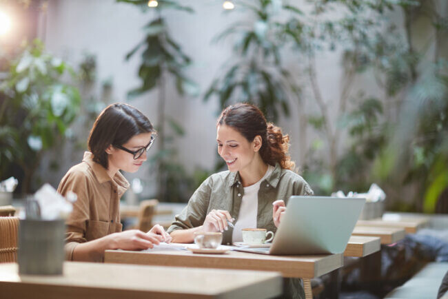 Portrait of two cheerful young omen enjoying work in beautiful outdoor cafe, copy space. Female Breadwinners