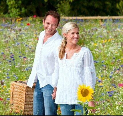 Couple on picnic in countryside walking in field of wild summer flowers