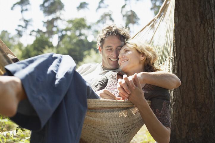 Couple sitting together in a hammock, smiling, in the sunshine