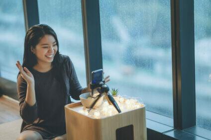 an asian chinese teenager girl vlogging in her room eating apple using her smart phone during raining day smiling date