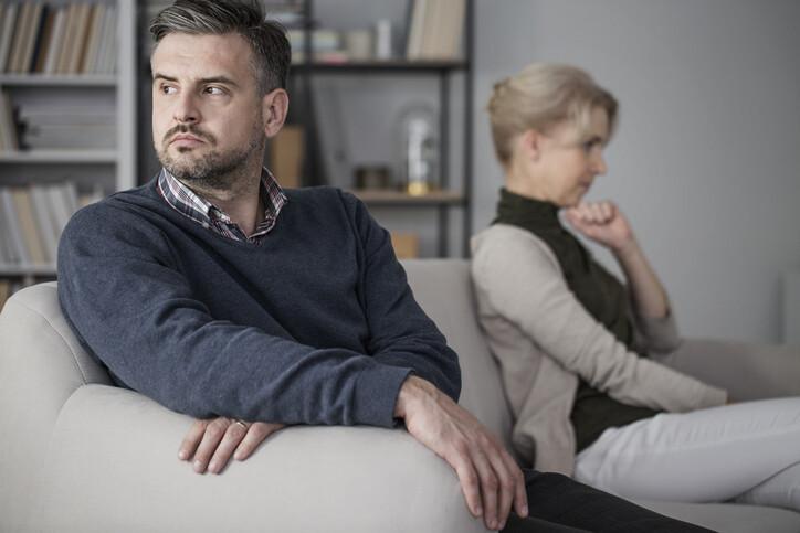 Men and woman sitting on a white sofa separately after quarrel