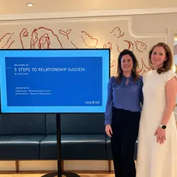Two Maclynn matchmakers standing in front of a screen before leading an expert masterclass. The text on the screen reads "5 Steps to Relationship Success".