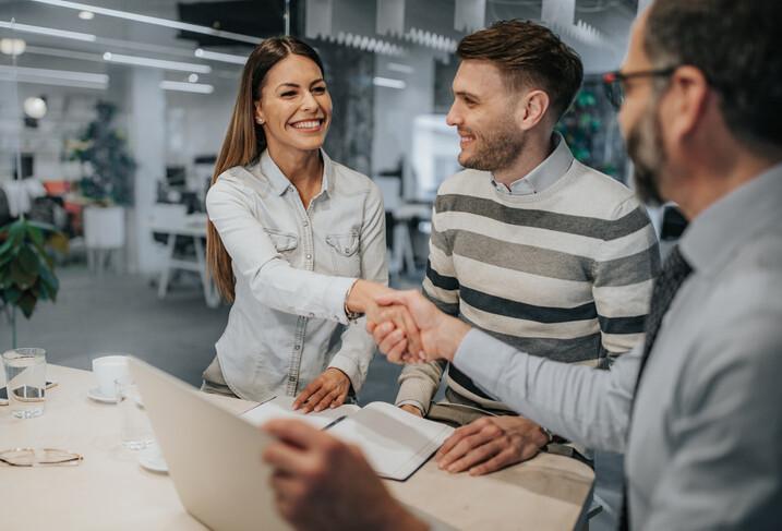 Happy couple came to an agreement with their insurance agent in the office. Focus is on woman shaking hands with an agent.