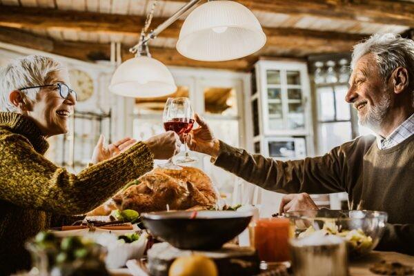 Happy mature couple toasting with wine while having Thanksgiving meal in dining room. to say thank you