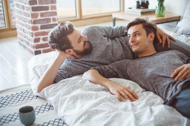 Male gay couple relaxing on a bed together, smiling at each other