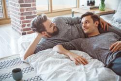 Male gay couple relaxing on a bed together, smiling at each other