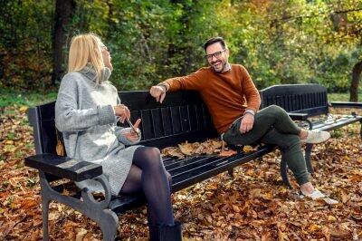 Woman and man in social distancing flirting sitting on a park bench for an outdoor date