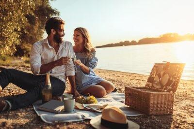 A young couple cheering with champagne at the beach with a picnic of romance