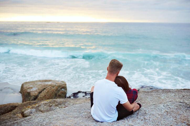 Shot of a happy young couple relaxing on a rock together at the beach