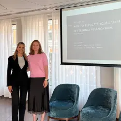 Two Maclynn matchmakers stand in front of a screen with two velvet armchairs underneath. The matchmakers are leading a masterclass on "How to Replicate Your Career Success in Personal Relationships."