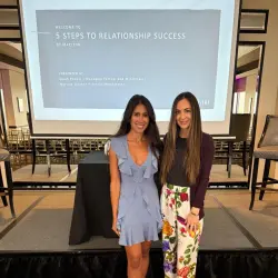 Two Maclynn matchmakers stand in front of a screen and stage before giving an expert masterclass. The screen reads "5 Steps to Relationship Success".