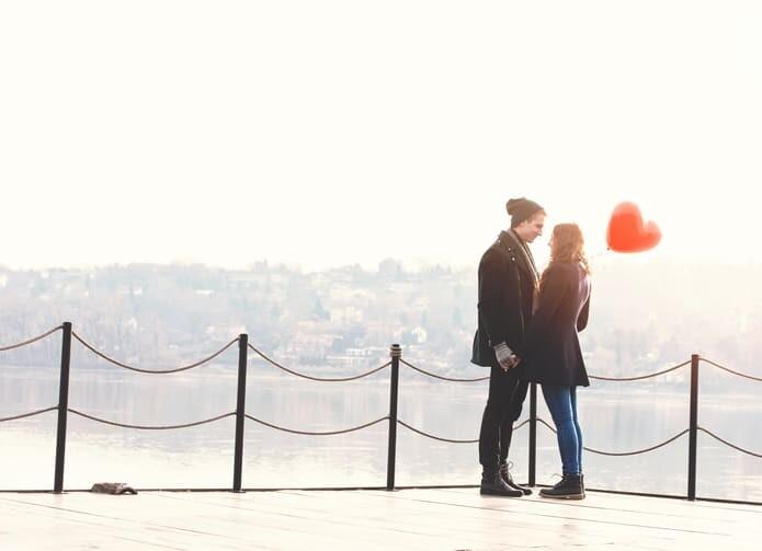 Young couple in love, at the riverside, with a red balloon