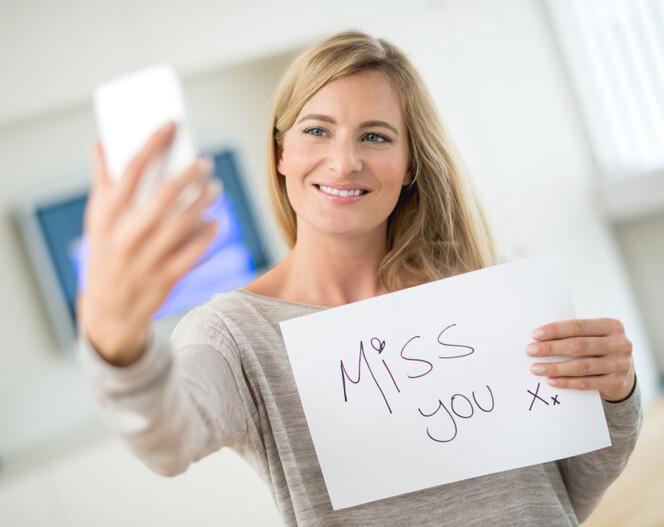 Woman talking on web chat through her phone holding a sign saying "miss you" - distance relationship concepts