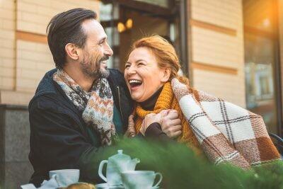 Happy middle-aged dating couple is relaxing in cafeteria outdoors. They are hugging with love and laughing