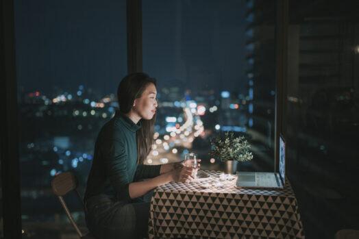 an asian chinese beautiful young lady having dessert in her apartment during magic hour, dusk and talking to her boyfriend thru internet using her laptop to online dating