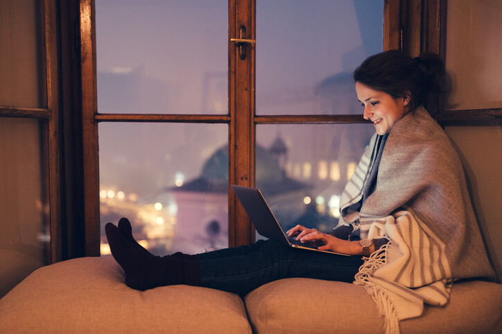 Young woman sitting at the window sill during a positive virtual date.